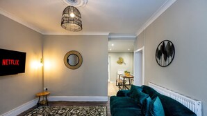 A living room with a TV, a round mirror, a patterned rug, a green sofa, and a ceiling light fixture. - Comfortable 4-bed Home With Free Parking Wales (Mountain Ash)