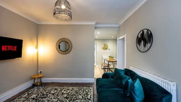 A living room with a TV, a round mirror, a patterned rug, a green sofa, and a ceiling light fixture.