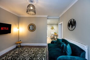 A living room with a TV, a round mirror, a patterned rug, a green sofa, and a ceiling light fixture. - Comfortable 4-bed Home With Free Parking Wales (Mountain Ash)