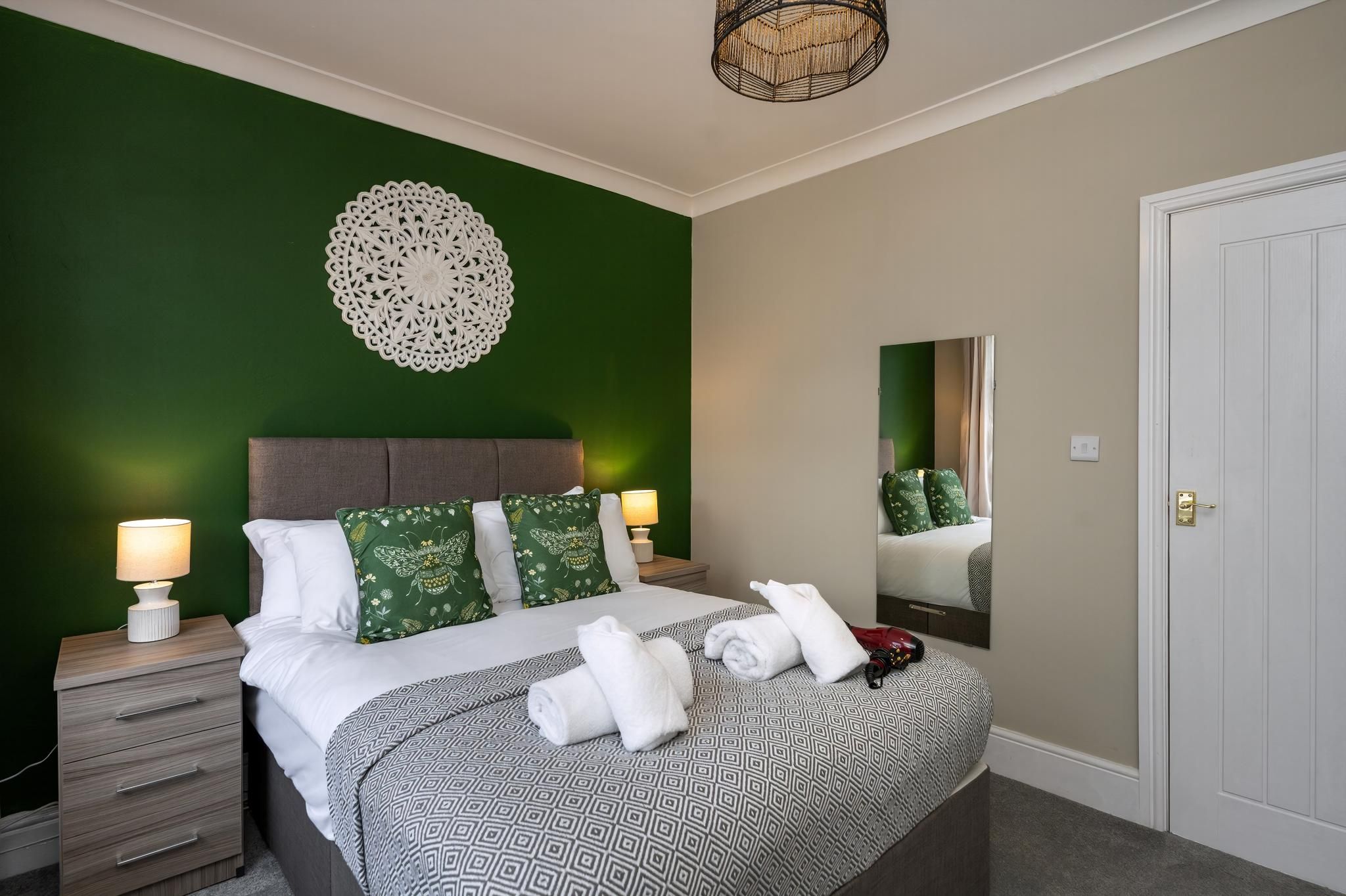 A hotel room with a bed, bedside lamps, a decorative wall piece, a mirror, and a door.