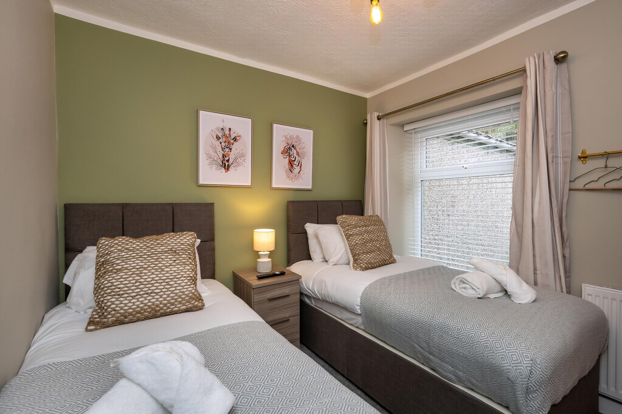 A hotel room with two beds, a nightstand with a lamp, and artwork on the wall.