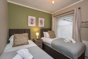 A hotel room with two beds, a nightstand with a lamp, and artwork on the wall. - Comfortable 4-bed Home With Free Parking Wales (Mountain Ash)