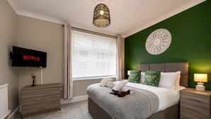 A bedroom with a bed, bedside tables, a TV, and a wall decoration. - Comfortable 4-bed Home With Free Parking Wales (Mountain Ash)