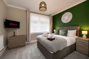 A bedroom with a bed, bedside tables, a TV, and a wall decoration. - Comfortable 4-bed Home With Free Parking Wales (Mountain Ash)