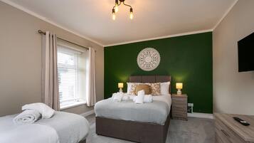 Une chambre d’hôtel comprenant un lit, un petit lit, une table de chevet avec une lampe, une commode et un téléviseur fixé au mur.