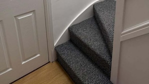 A staircase with a textured carpet leading to a landing with a coat rack. - Sea Breeze 1-bed Retreat With Parking (Swansea)