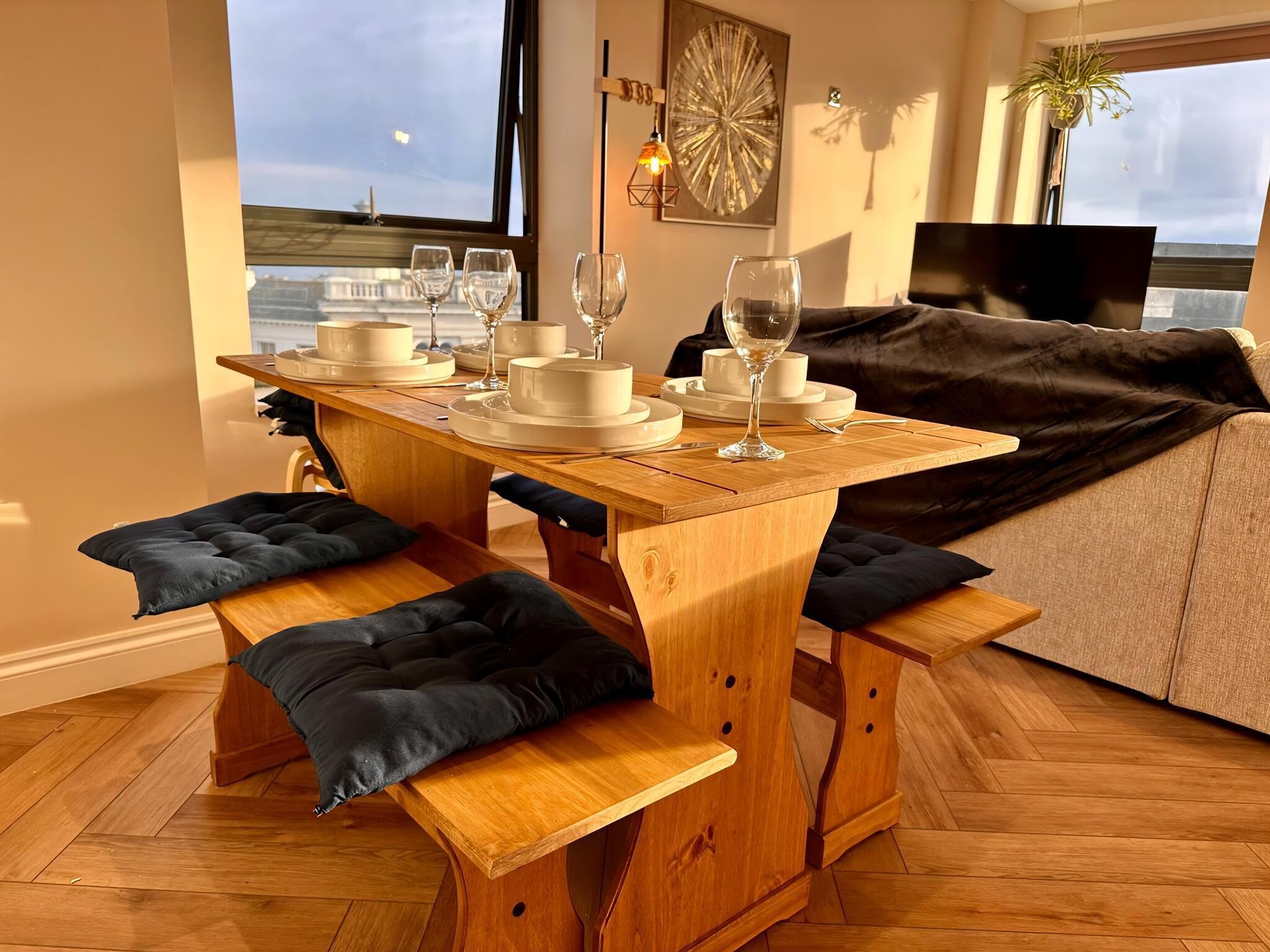 Une table à manger avec des bancs, un canapé et un téléviseur dans un salon offrant une vue sur la ville.