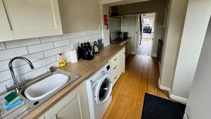 A compact kitchen with a sink, washing machine, and wooden countertop. - Cosy 2 Bedroom Home With Parking Near City Centre (Swansea)