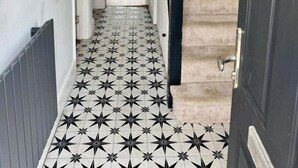 A hallway with a black and white star-patterned floor, a white door, and a staircase with beige carpet. - Cosy 2 Bedroom Home With Parking Near City Centre (Swansea)