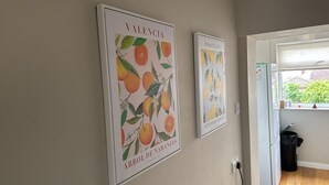 A hallway with two framed posters on the wall, a window with a view of greenery, and a door leading to another room. - Cosy 2 Bedroom Home With Parking Near City Centre (Swansea)