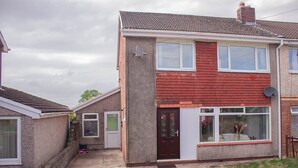 A two-story house with a red brick facade, a front door, and a small front yard. - Swansea 3 Bedroom Home With Parking & Garden (Swansea)
