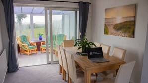 A dining area with a laptop displaying 'Tailored Accommodation', a wooden table, and chairs. - Swansea 3 Bedroom Home With Parking & Garden (Swansea)