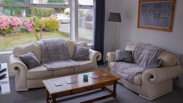 A living room with two beige sofas, a wooden coffee table, and a painting on the wall. - Swansea 3 Bedroom Home With Parking & Garden (Swansea)