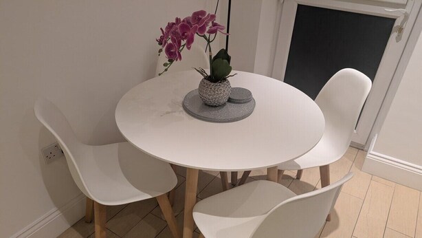 A round white table with four white chairs, a small plant in a textured pot, and a blue rug on the floor. - City Escape 1 Bedroom Flat in Swansea Centre (Swansea)