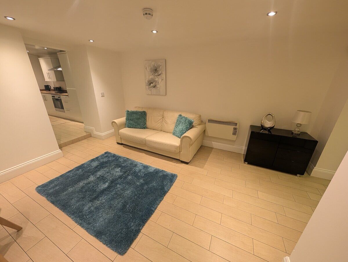 A living room with a beige sofa, a blue rug, a black cabinet, and a painting on the wall.