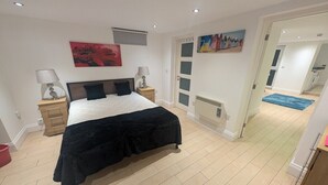 A bedroom with a bed, bedside tables, a nightstand, a radiator, and a door leading to another room. - City Escape 1 Bedroom Flat in Swansea Centre (Swansea)