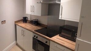 A compact kitchen with a built-in stove, microwave, and oven. There is a wooden countertop and a stainless steel range hood. - City Escape 1 Bedroom Flat in Swansea Centre (Swansea)
