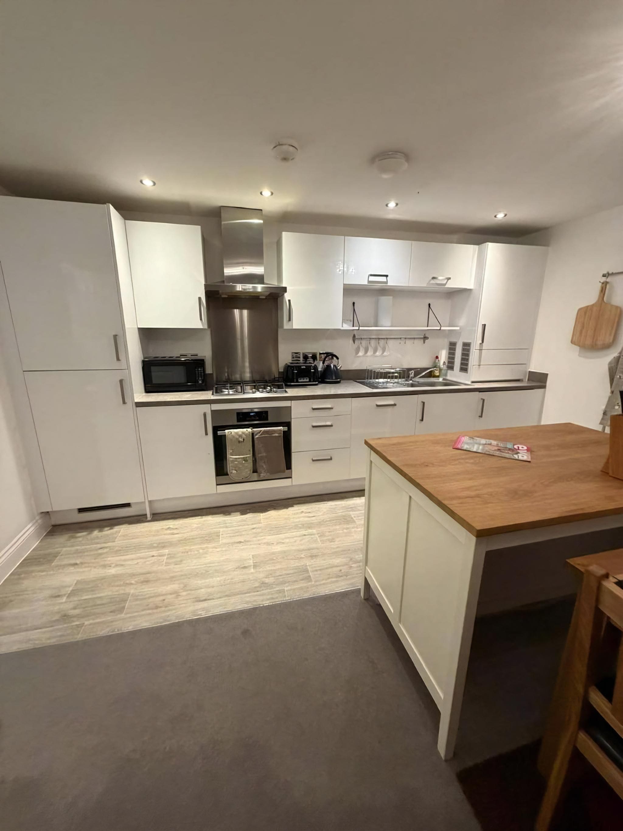 A modern kitchen with white cabinets, a wooden island, stainless steel appliances, and a pizza stone.
