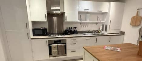 A modern kitchen with white cabinets, a wooden island, stainless steel appliances, and a pizza stone.