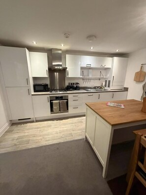 A modern kitchen with white cabinets, a wooden island, stainless steel appliances, and a pizza stone. - Reading Retreat 1 Bed With Private Parking (Reading)