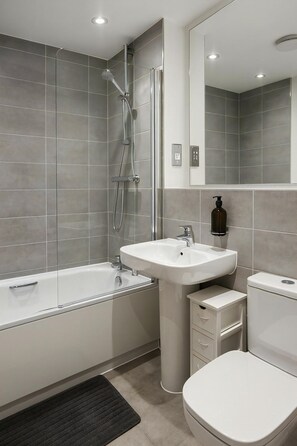 A modern bathroom with a bathtub, sink, toilet, and a mirror. - Reading Retreat 1 Bed With Private Parking (Reading)