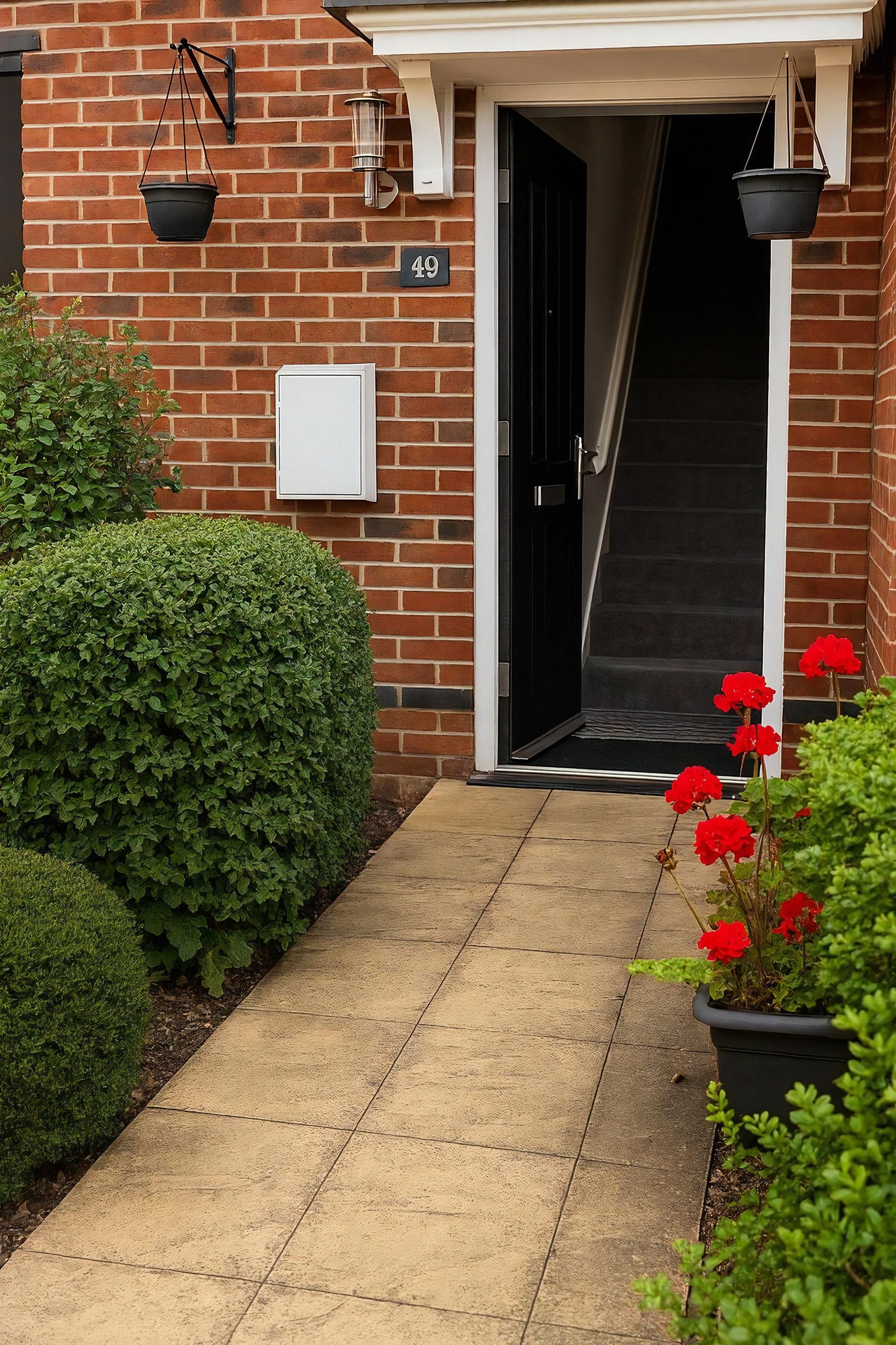 A brick building with a number '49' sign, a black door, a white mailbox, and a pathway leading to the entrance.