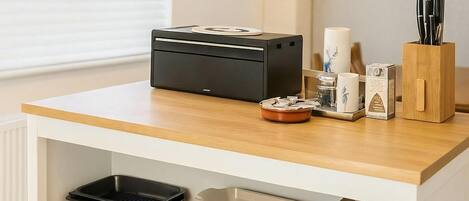 A kitchen area with a countertop, a black appliance, a white container, and a wooden utensil holder.