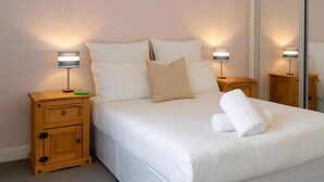 A neatly made bed with white linens, two bedside lamps, a wooden nightstand with a drawer, and a mirror on the wall. - Reading Retreat 1 Bed With Private Parking (Reading)