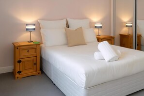 A neatly made bed with white linens, two bedside lamps, a wooden nightstand with a drawer, and a mirror on the wall. - Reading Retreat 1 Bed With Private Parking (Reading)