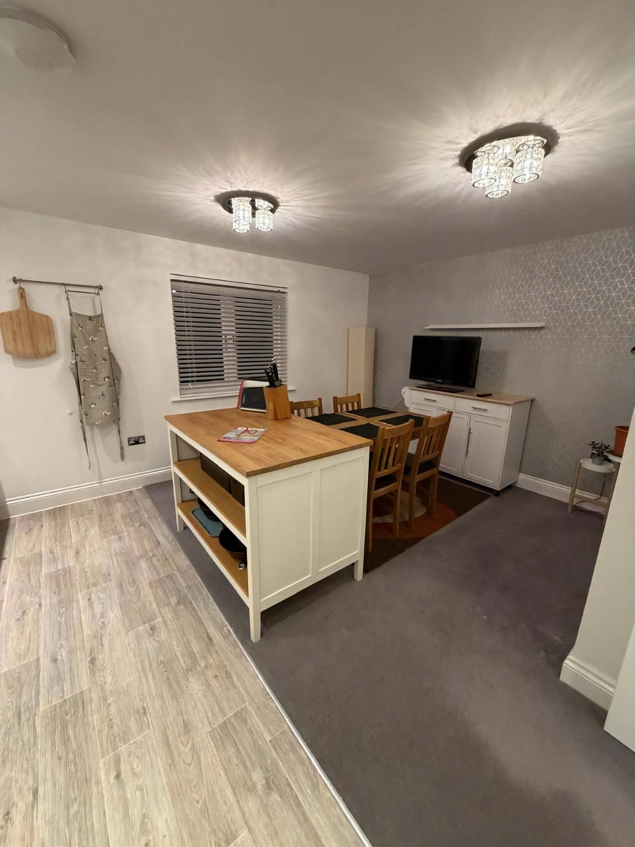 A compact kitchen with a dining area, wooden flooring, and a ceiling light fixture.