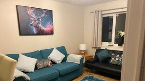 Ein Wohnzimmer mit einem türkisfarbenen Sofa, einem schwarzen Sofa, einem blauen Teppich und einem Bild eines Rehs an der Wand.