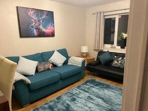 Ein Wohnzimmer mit einem türkisfarbenen Sofa, einem schwarzen Sofa, einem blauen Teppich und einem Bild eines Rehs an der Wand.