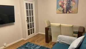 Ein Wohnzimmer mit einem petrolfarbenen Sofa, einem Couchtisch, einem an der Wand montierten Fernseher und einer Glastür.