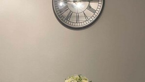 Ein Essbereich mit einer runden Wanduhr, einem kleinen Tisch mit zwei Stühlen und einer Blumenvase.