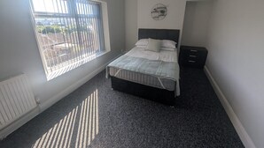 Une chambre à coucher avec un lit, une fenêtre avec des stores, un radiateur et une table de chevet.