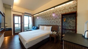 Quarto de hotel com uma cama grande, uma mesinha de cabeceira com telefone, uma mesinha de vime e vista para o exterior através de uma porta deslizante.