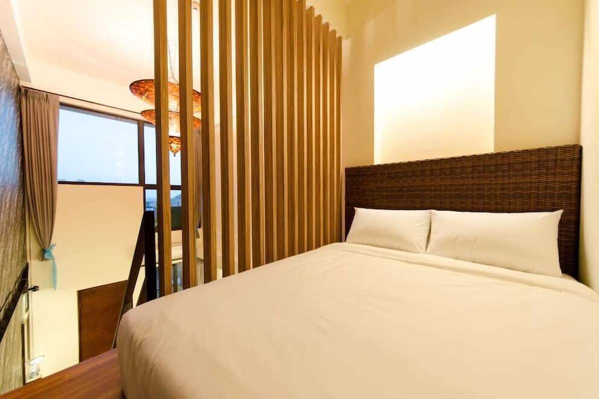 A hotel room with a large bed, a view through a window, and a vertical wooden panel.