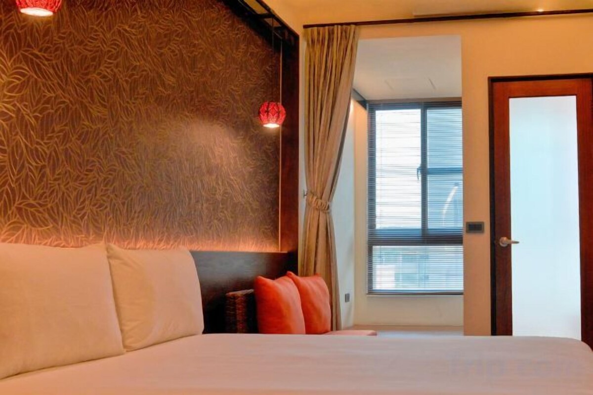 A hotel room with a bed, a patterned wall, a window with curtains, and a door.