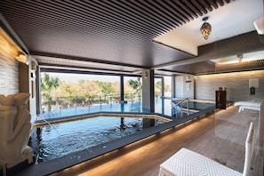 A modern indoor swimming pool with clear views of the surrounding landscape, a wooden deck, and a stone wall. - Si Anping by Hotel Si (Tainan)