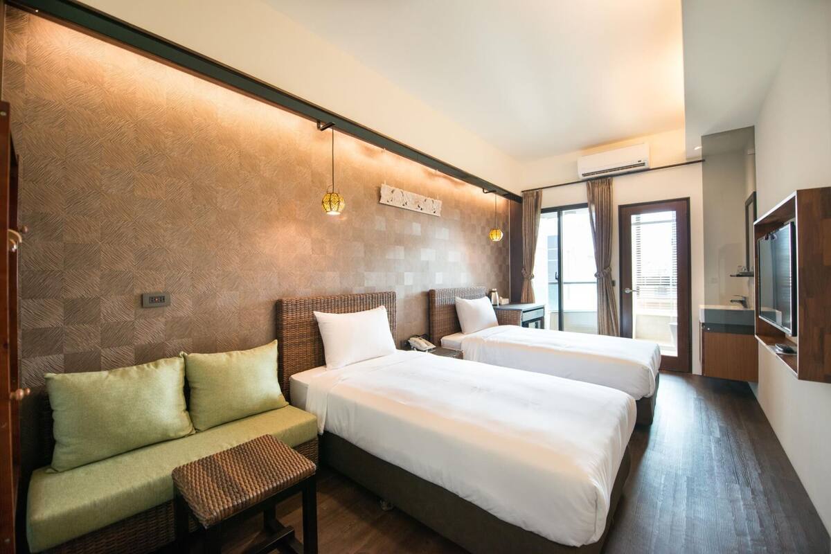 A hotel room with two beds, a sofa, a small table, a TV, and a window with curtains.