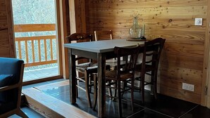 A wooden interior with a dining table and chairs, a hanging light fixture, and a view through a glass door. - Gîte Le Gyr - Pays des Ecrins (Vallouise-Pelvoux)