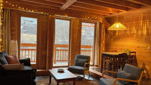 A cozy cabin interior with wooden walls, a dining area, and large windows. - Gîte Le Gyr - Pays des Ecrins (Vallouise-Pelvoux)