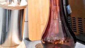 A kitchen counter with a stainless steel knife block, a wooden cutting board, and a copper-colored vase.
