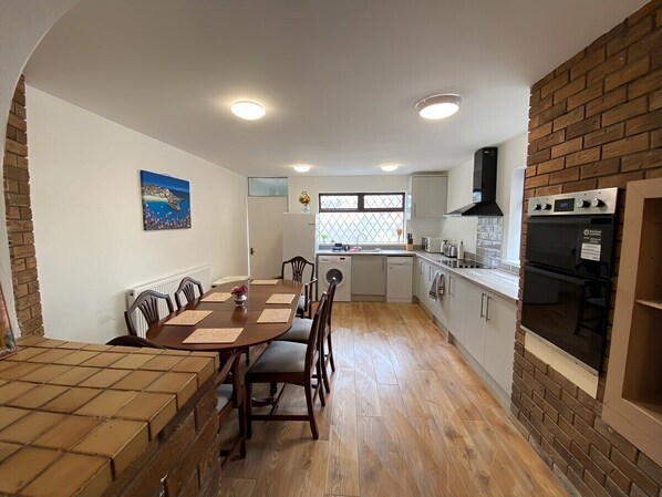 Une cuisine compacte avec un coin repas, un plancher en bois et un mur d’accent en briques.