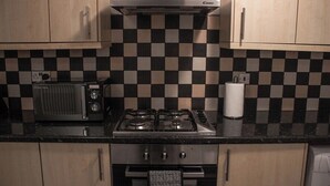 A kitchen with a checkered backsplash, a stove, and a microwave. - Family-friendly 3-bed House in Swansea (Swansea)