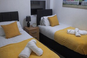A hotel room with two beds, each with a yellow blanket and white pillows. There is a nightstand with a lamp and a clock. - Family-friendly 3-bed House in Swansea (Swansea)