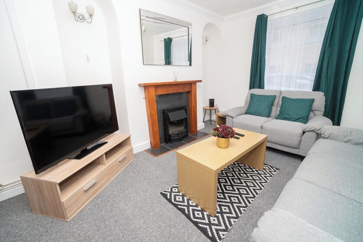 A modern living room with a flat-screen TV, a fireplace, a sofa, and a patterned rug.