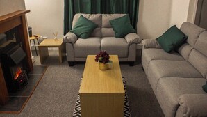 A living room with a beige sofa, a wooden coffee table, and a fireplace. - Family-friendly 3-bed House in Swansea (Swansea)