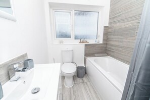 A modern bathroom with a white toilet, a bathtub, and a sink. - Family-friendly 3-bed House in Swansea (Swansea)