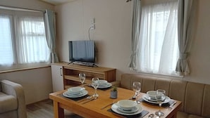 Ruokailutila, jossa on puinen pöytä, johon on katettu neljälle, jalustalla oleva televisio ja taustalla oleva sohva.